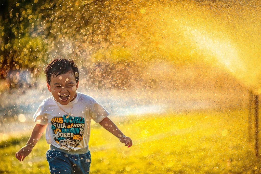 Lachend kind dat door waterdruppels loopt op een zonnige dag
